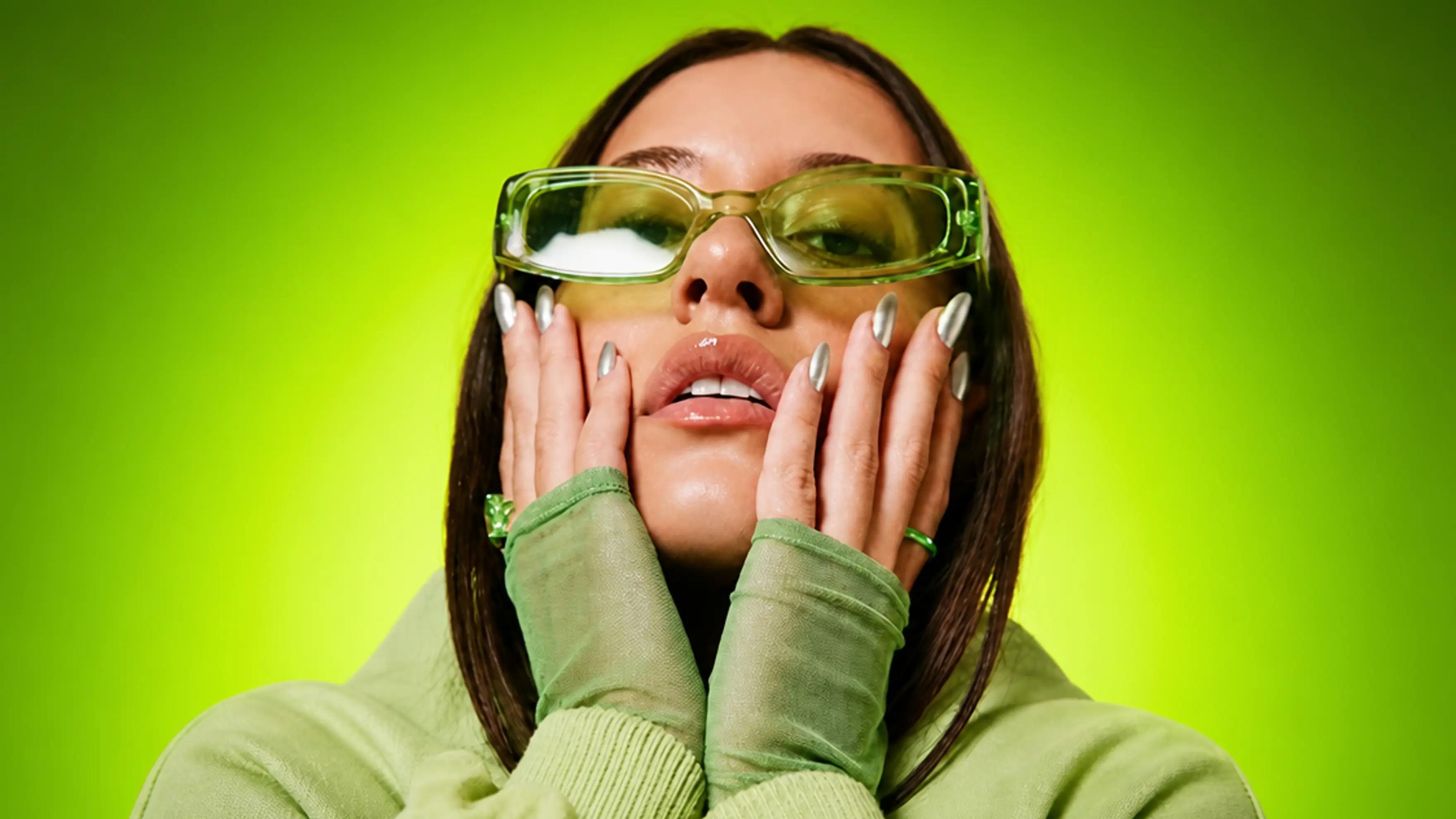 Close-up portrait of a fashion virtual model wearing translucent green sunglasses on a vibrant green studio background